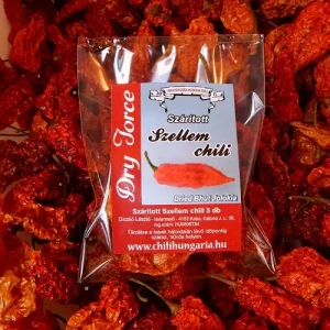 Clear plastic bag of dried Bhut Jolokia ghost chilies against a background of red peppers; label reads 'Dried Bhut Jolokia' and 'Szárított Szellem chili'.